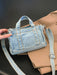 denim shoulder bag, light blue, held at an angle by a woman's hand, atop a camel colored overcoat