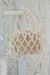 pearl polyester crossbody handbag, white pearls, hanging on a white doorknob against a textured white wall