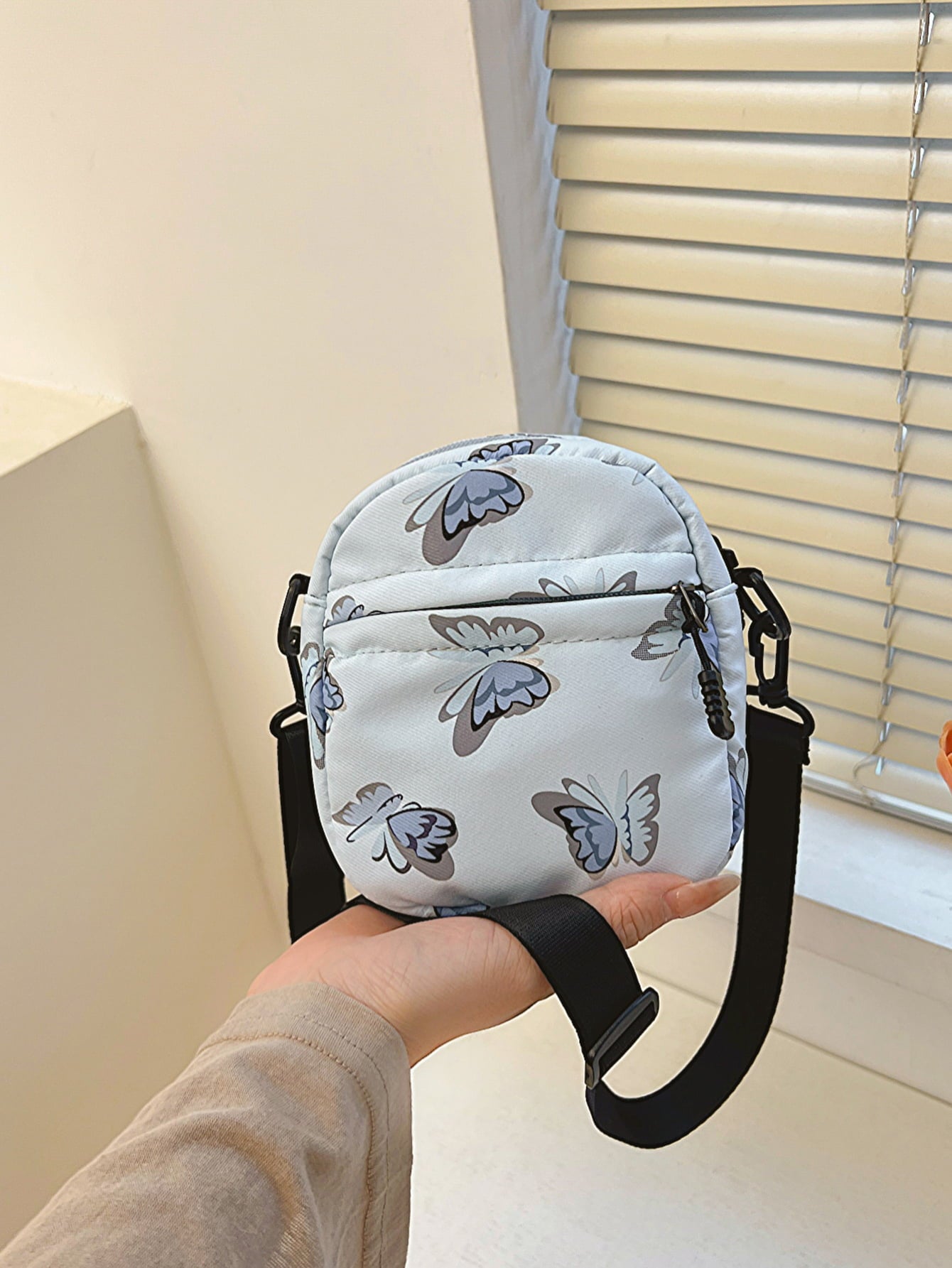 butterfly print polyester shoulder handbag, blue with blue butterflies, held at arm's length in the palm of a woman's hand