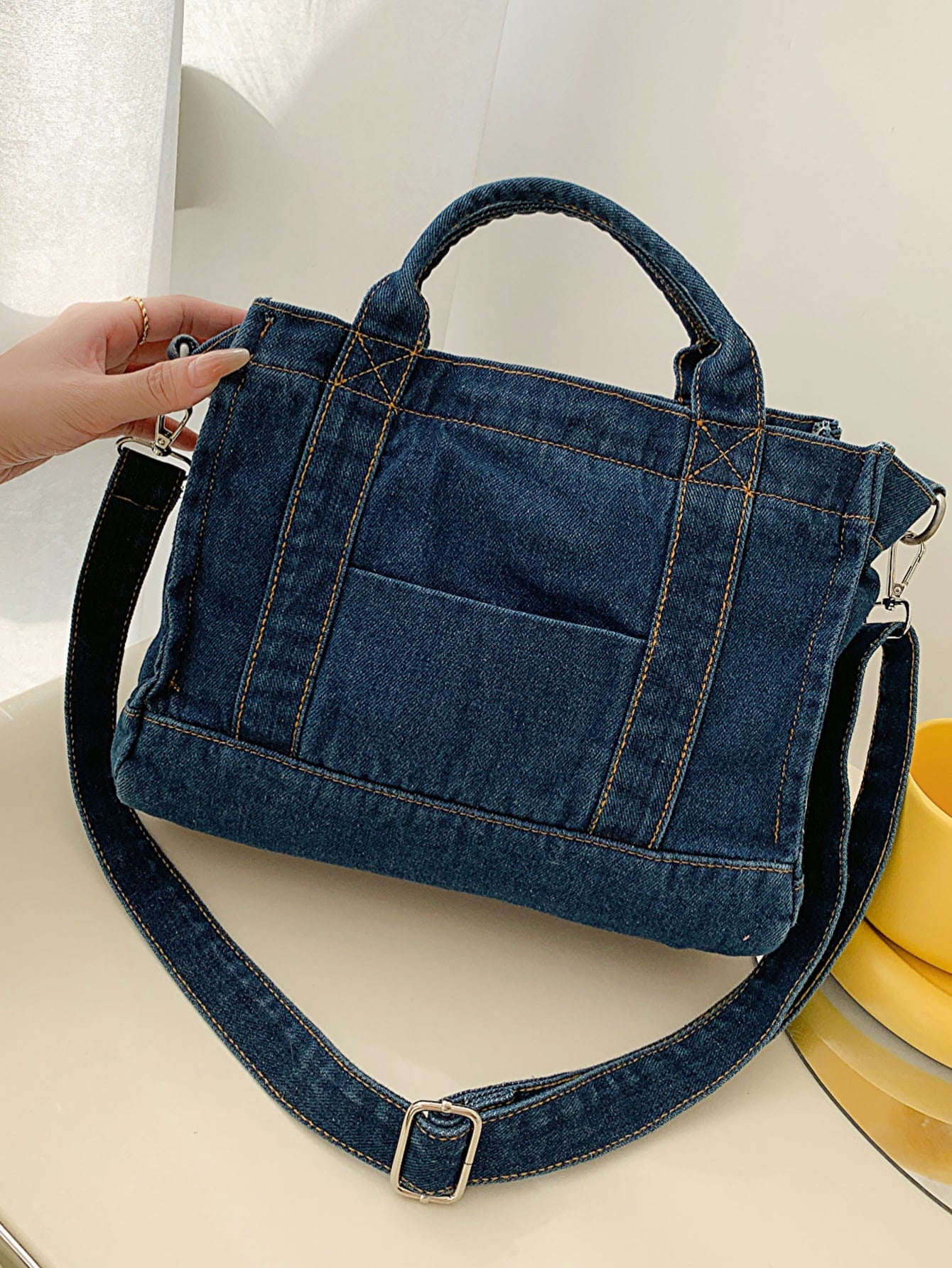 denim shoulder handbag, dark blue, tilted view, woman's hand on left side