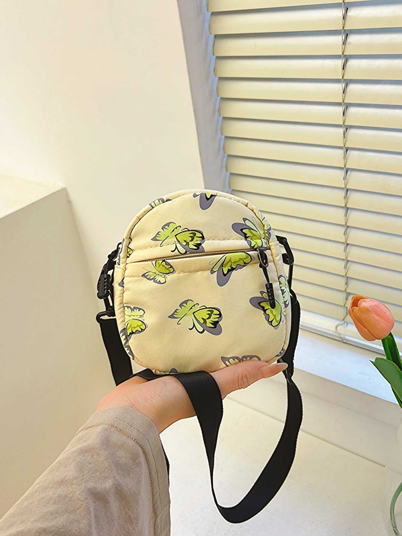 butterfly print polyester shoulder handbag, yellow with green butterflies, held at arm's length in a woman's palm