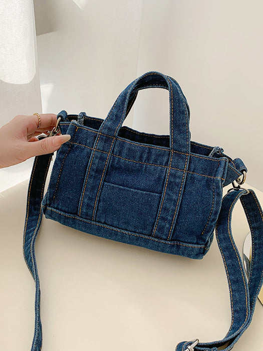 denim shoulder handbag, dark blue, angled view, held by woman's hand