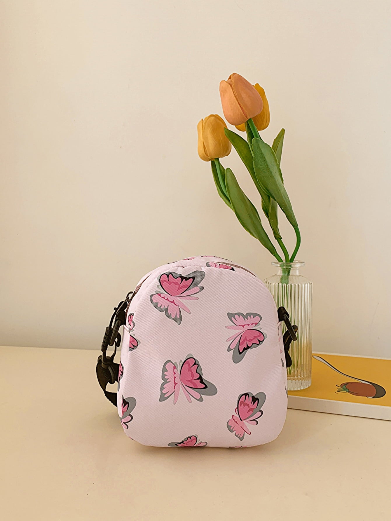 butterfly print polyester shoulder handbag, pink with pink butterflies, back view, on counter with yellow tulips