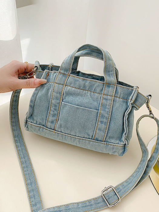 denim shoulder handbag, light blue, held at an angle by a woman's hand on a white countertop