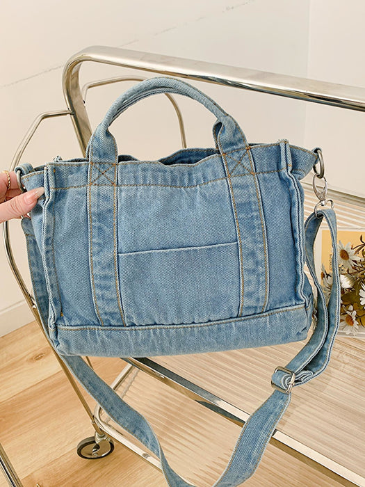 denim shoulder handbag, light blue, held at an angle in a woman's hand atop a glass and metal slatted cart