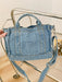denim shoulder handbag, light blue, held at an angle in a woman's hand atop a glass and metal slatted cart